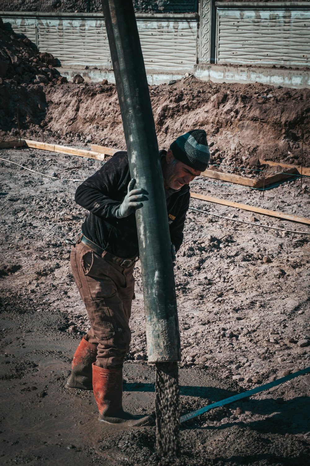 Worker guiding a concrete pump hose over prepared ground